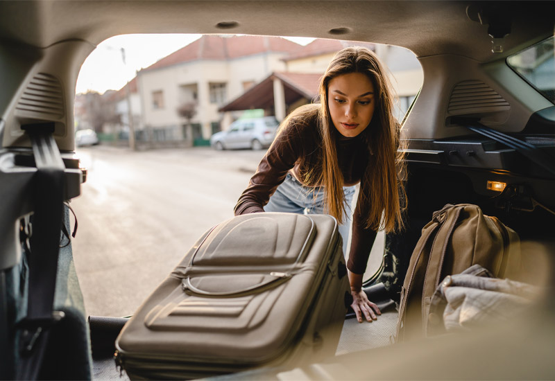 Young woman packing suitcase into car